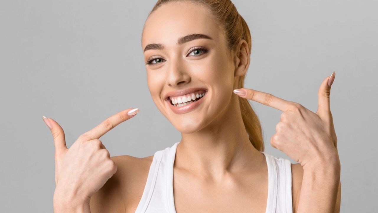 Mulher jovem apontando para seu sorriso perfeito com facetas de porcelana